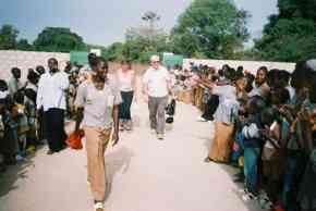 Pippa and Ian walk towards Bakalarr School between lines of clapping children