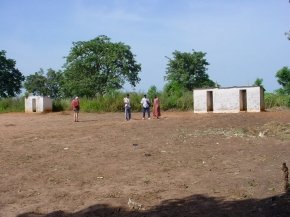 distant view across the sandy school grounds of two small white painted buildings