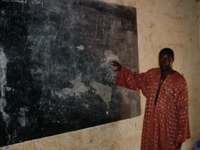 a teacher shows the blackboard which has large patches of its black surface missing