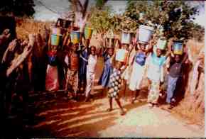 children and villagers bring water in buckets on their heads