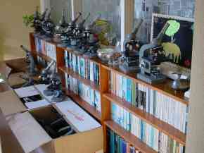 A row of optical microscopes stands on a bookcase awaiting packing