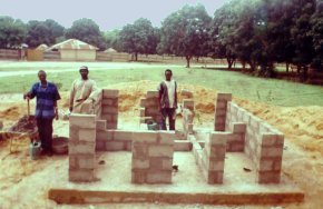 concrete block walls being built on the base slab, reaching about waist height so far