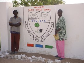 the two artists, Ousman and the art teacher, stand on either side of the painting on this panel which is the school badge